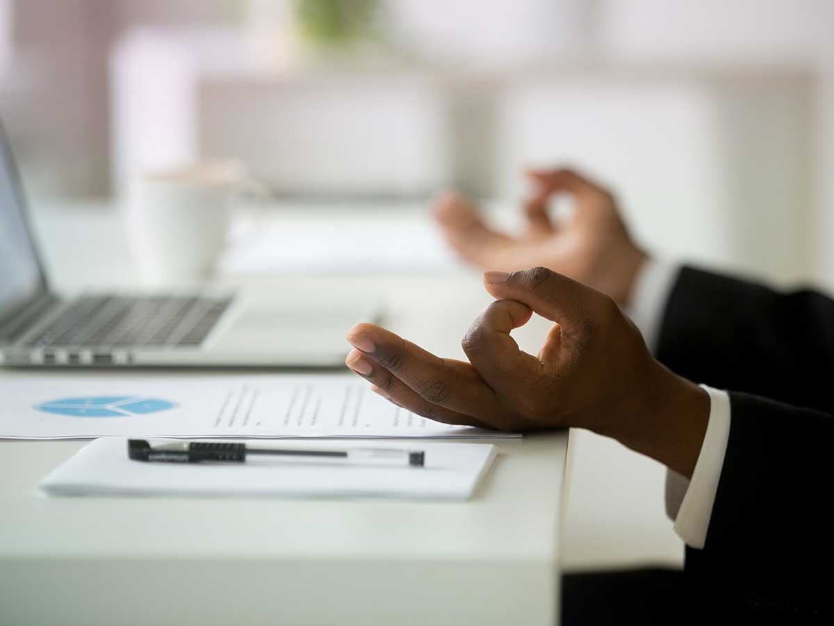 Close up of the hands of a African american businessman in mudra position, relaxing and meditating at work desk in an office