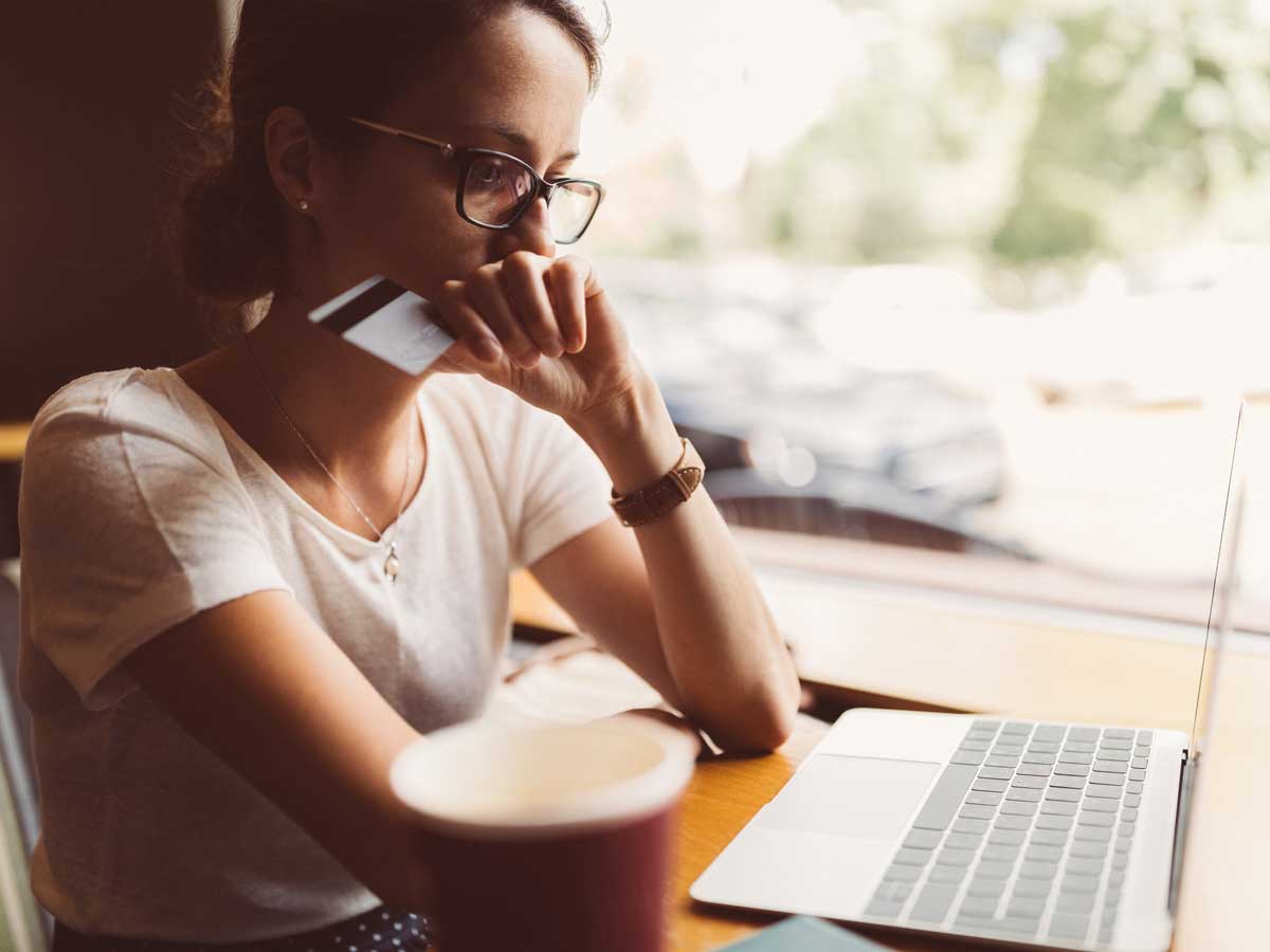 Woman sitting at desk looking at laptop holding her credit card