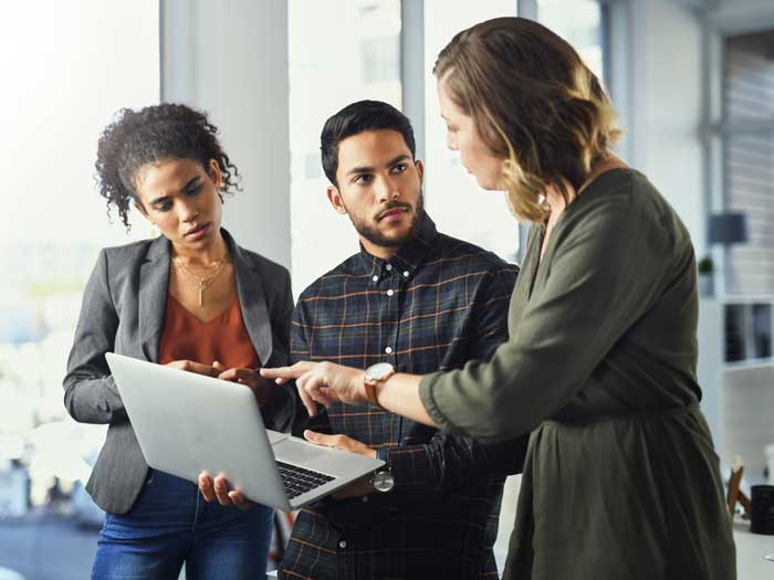 Three of business people, standing by a window in an office building, having a discussion over a laptop