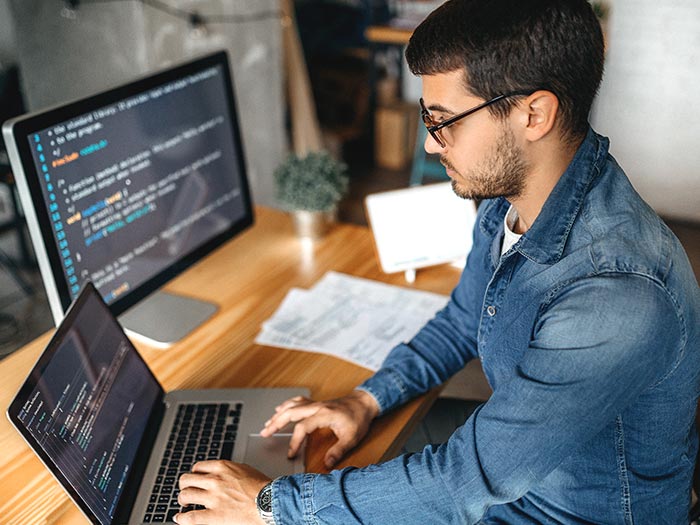 Person working at a desk with a laptop and multiple monitors