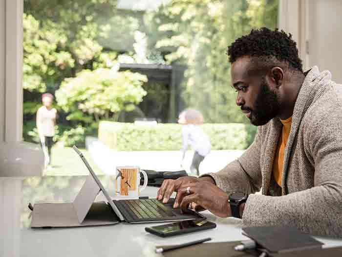 A man works from home on his digital tablet while his children play in the background.