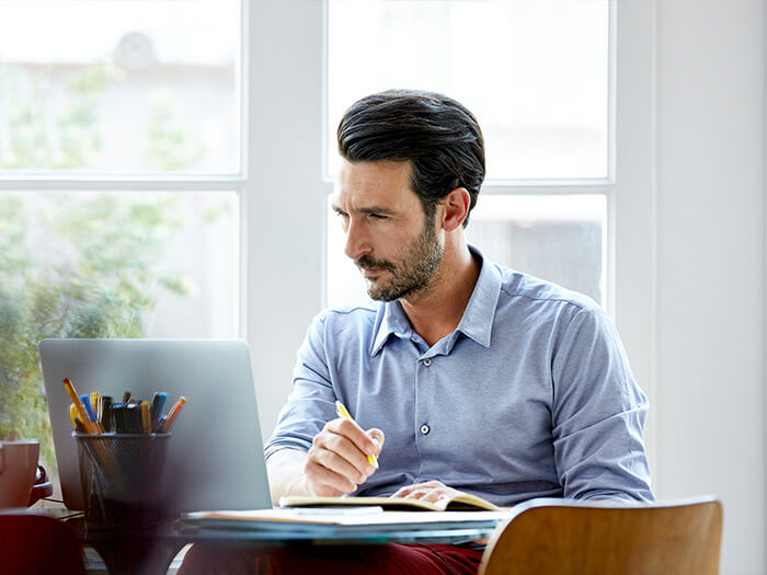 Businessman writing notes while using a laptop