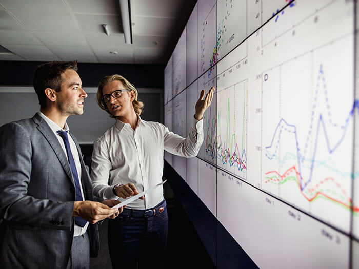 Business professionals standing in front of large screen displaying data