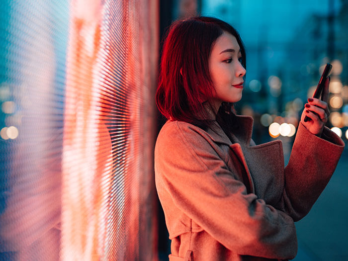 Young Woman With Smartphone Standing Against A Digital Display