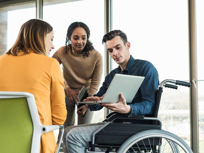  Un jeune homme d'affaires en fauteuil roulant montre un ordinateur portable à un collègue dans un bureau.