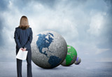 Business woman holding papers behind her back and looking at different coloured globes.